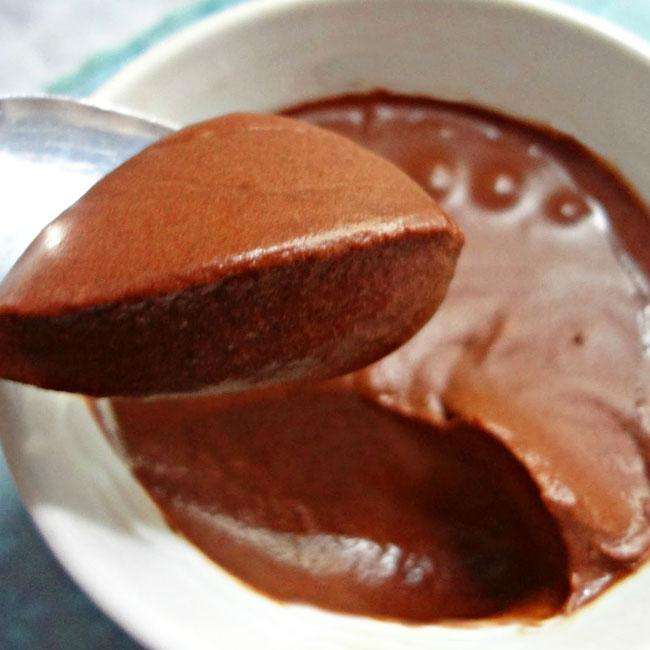 Mousse de Chocolate Diet dentro de um recipiente branco redondo, com uma porção do mousse em uma colher de inox.