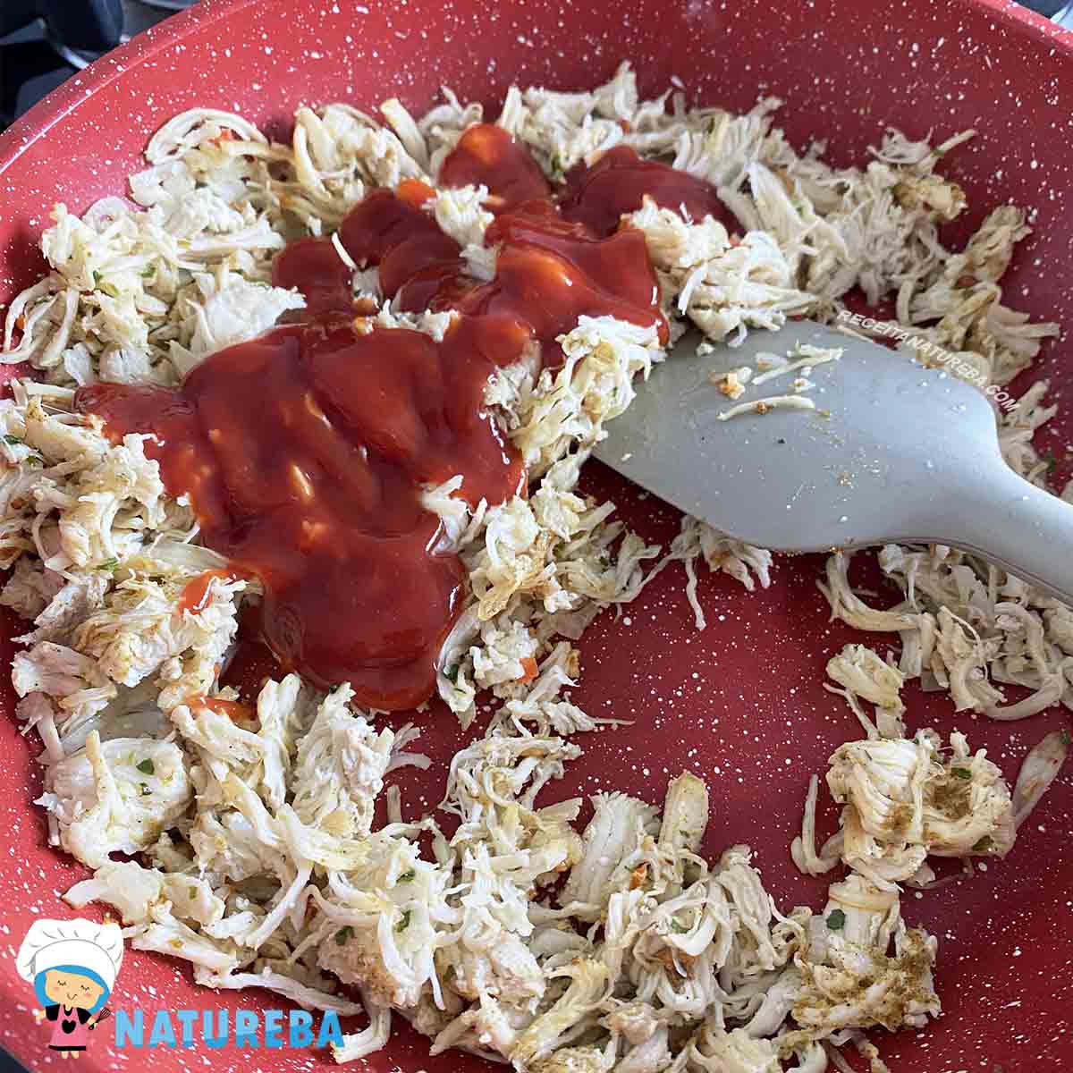 juntando o frango desfiado com o molho de tomate na panela com a cebola refogada